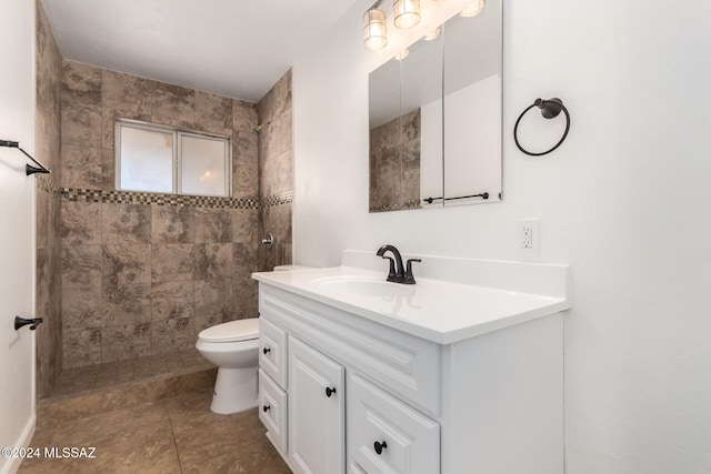 bathroom featuring a tile shower, tile patterned flooring, vanity, and toilet