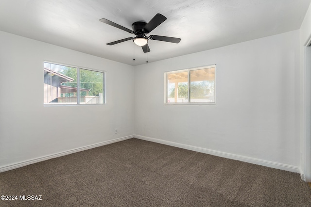 empty room with dark carpet, ceiling fan, and a healthy amount of sunlight