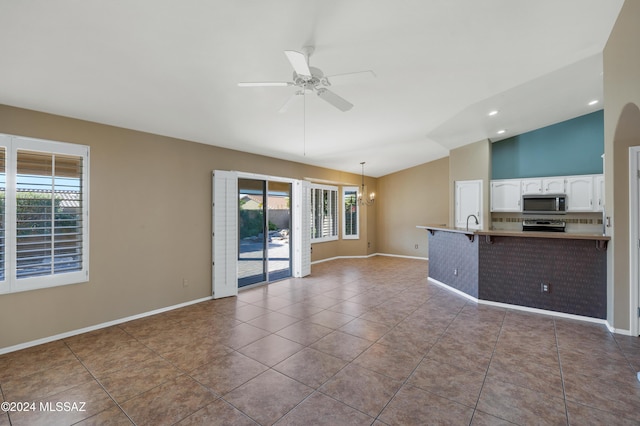 unfurnished living room with tile patterned flooring, ceiling fan with notable chandelier, and lofted ceiling