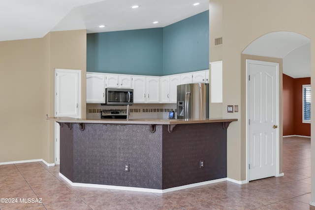 kitchen featuring a high ceiling, white cabinets, appliances with stainless steel finishes, kitchen peninsula, and a breakfast bar area