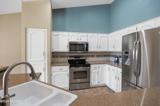 kitchen featuring backsplash, white cabinets, sink, light tile patterned floors, and appliances with stainless steel finishes