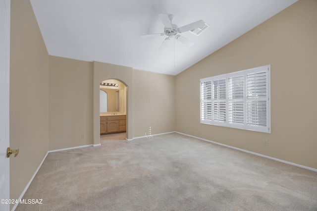 unfurnished bedroom featuring light carpet, connected bathroom, vaulted ceiling, and ceiling fan