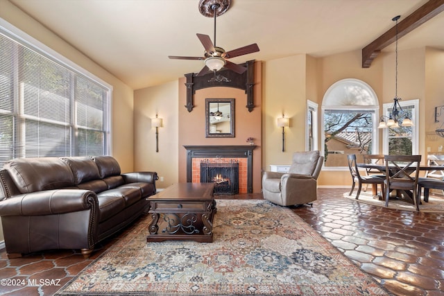 living room with vaulted ceiling with beams, ceiling fan with notable chandelier, a wealth of natural light, and a brick fireplace