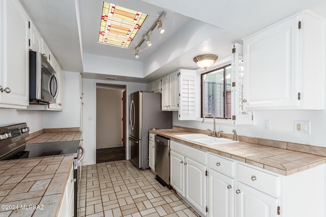 kitchen featuring tile countertops, white cabinets, sink, rail lighting, and appliances with stainless steel finishes