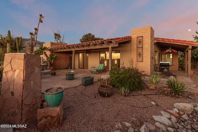 back house at dusk featuring ceiling fan and a patio