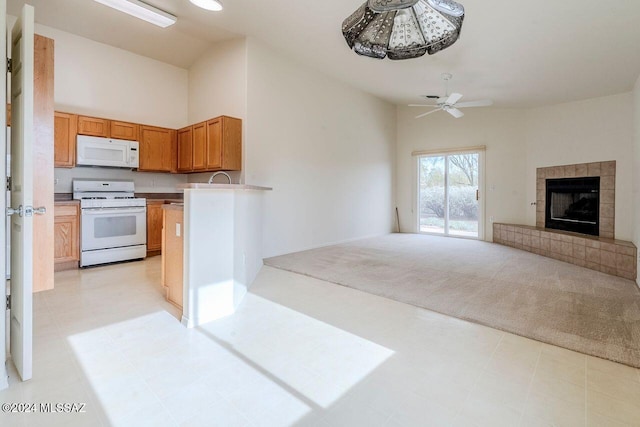 kitchen featuring light carpet, kitchen peninsula, white appliances, ceiling fan, and a tiled fireplace