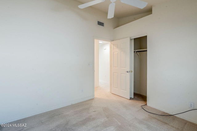 unfurnished bedroom with ceiling fan, light colored carpet, a towering ceiling, and a closet