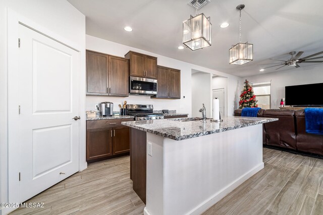 kitchen featuring a kitchen island with sink, hanging light fixtures, light stone countertops, and appliances with stainless steel finishes