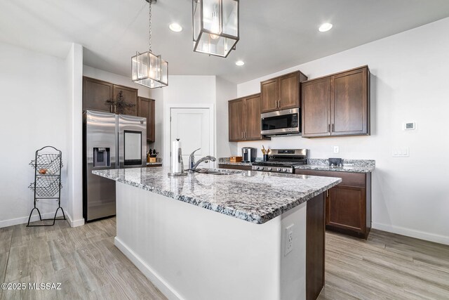 kitchen with sink, hanging light fixtures, light wood-type flooring, appliances with stainless steel finishes, and an island with sink