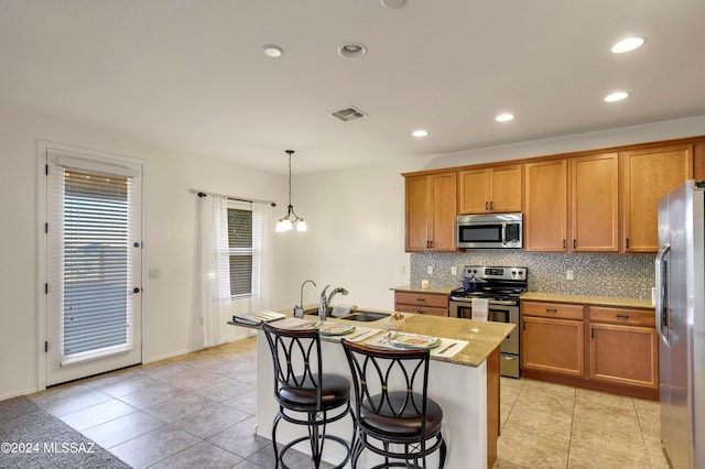 kitchen featuring sink, an island with sink, appliances with stainless steel finishes, decorative light fixtures, and light tile patterned flooring