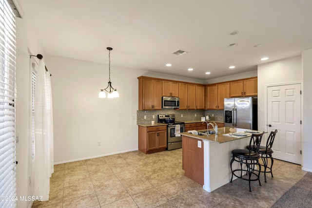 kitchen featuring decorative backsplash, appliances with stainless steel finishes, a breakfast bar, decorative light fixtures, and an island with sink