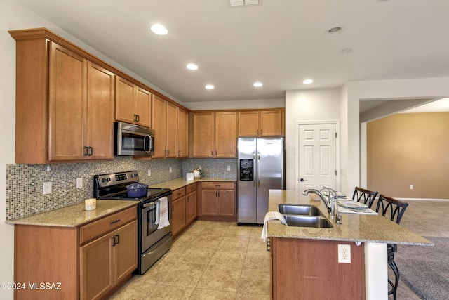 kitchen with light stone countertops, sink, backsplash, a kitchen bar, and appliances with stainless steel finishes