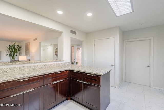 kitchen with kitchen peninsula, light stone countertops, and dark brown cabinetry