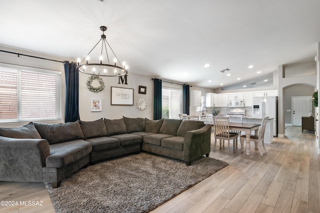 living room with a notable chandelier, lofted ceiling, and light hardwood / wood-style flooring