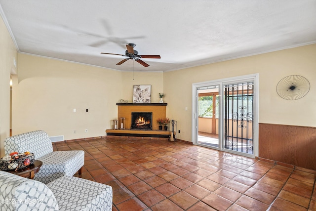 tiled living room with ceiling fan, wood walls, and ornamental molding