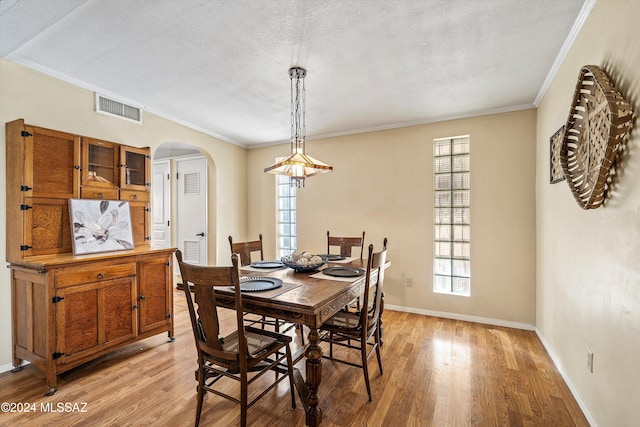 dining area featuring a textured ceiling, light wood-type flooring, and ornamental molding