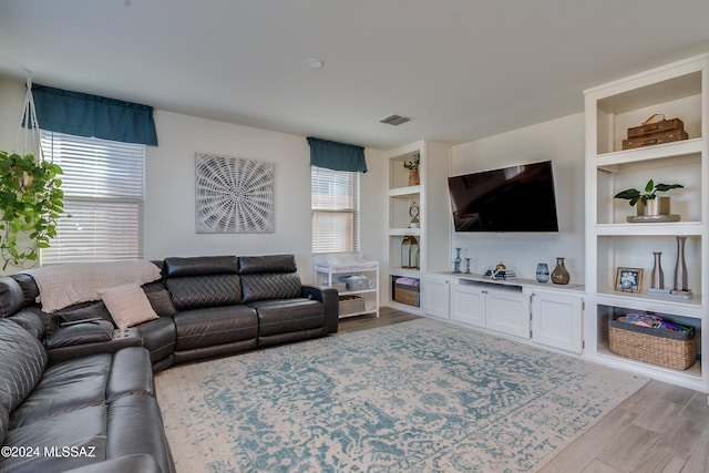 living room featuring built in shelves, a wealth of natural light, and light hardwood / wood-style flooring