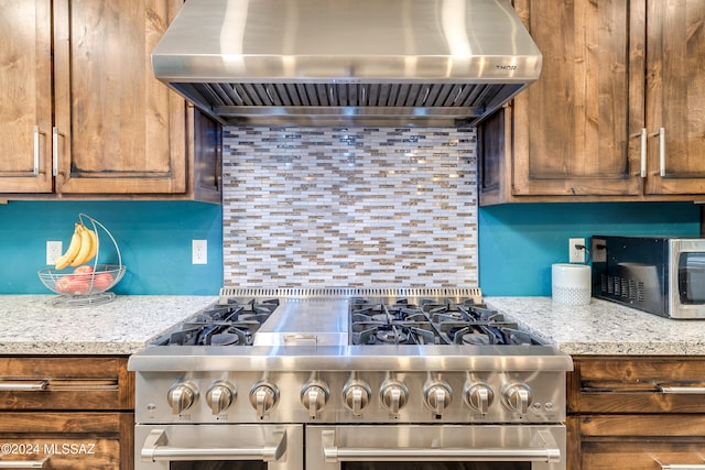 kitchen with backsplash, light stone countertops, wall chimney range hood, and stainless steel appliances