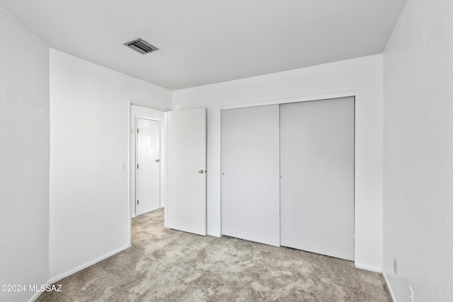 unfurnished bedroom with light colored carpet and a closet