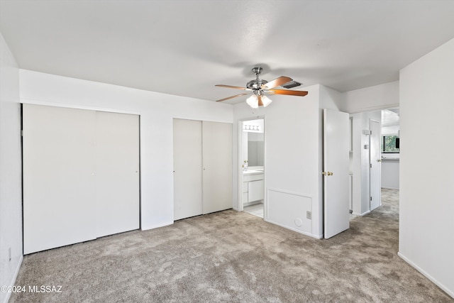 unfurnished bedroom with ceiling fan, light carpet, connected bathroom, and multiple closets