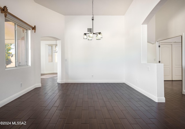 spare room featuring a towering ceiling, dark hardwood / wood-style floors, and a notable chandelier