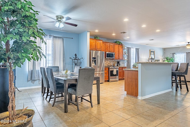 kitchen featuring appliances with stainless steel finishes, backsplash, a kitchen breakfast bar, ceiling fan, and light tile patterned floors