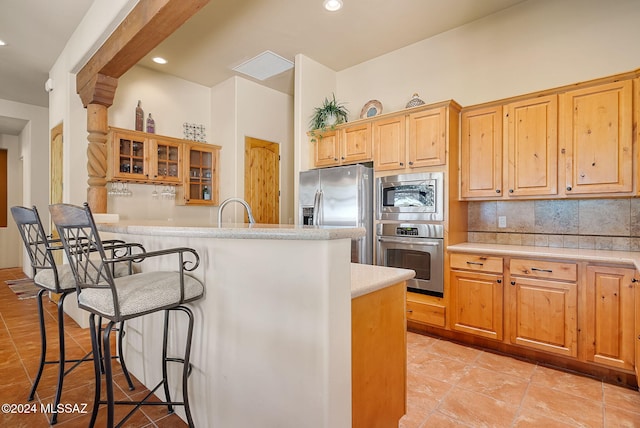 kitchen featuring light tile patterned floors, a kitchen breakfast bar, decorative backsplash, a kitchen island, and appliances with stainless steel finishes