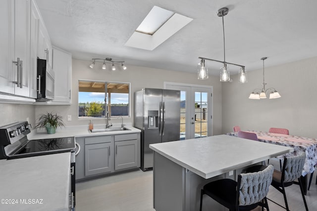 kitchen with gray cabinetry, sink, a kitchen breakfast bar, decorative light fixtures, and appliances with stainless steel finishes