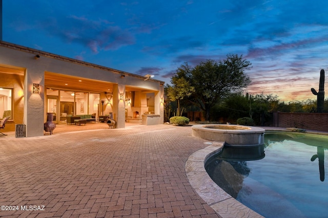 pool at dusk featuring an in ground hot tub, exterior fireplace, and a patio area