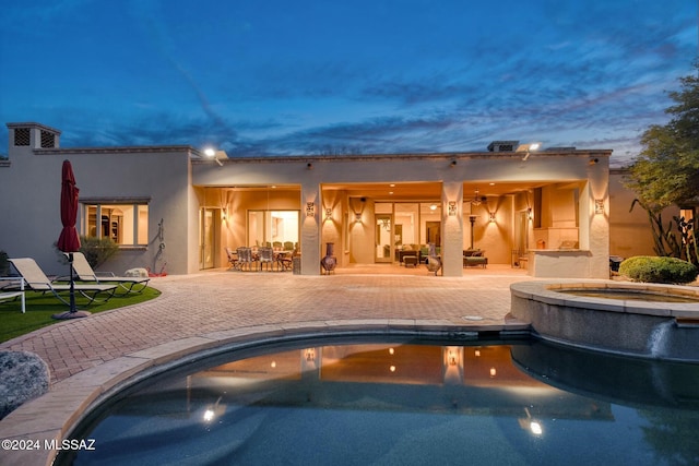 pool at dusk with a patio area and an in ground hot tub