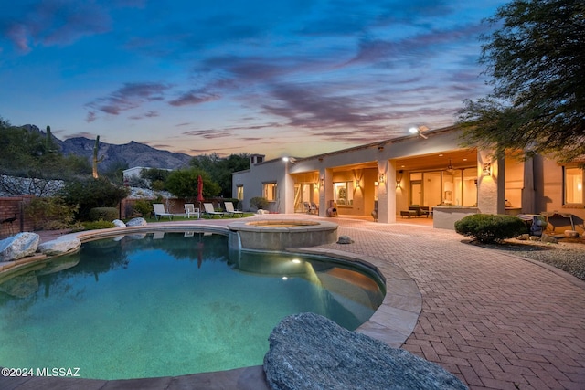 pool at dusk with a mountain view, an in ground hot tub, and a patio