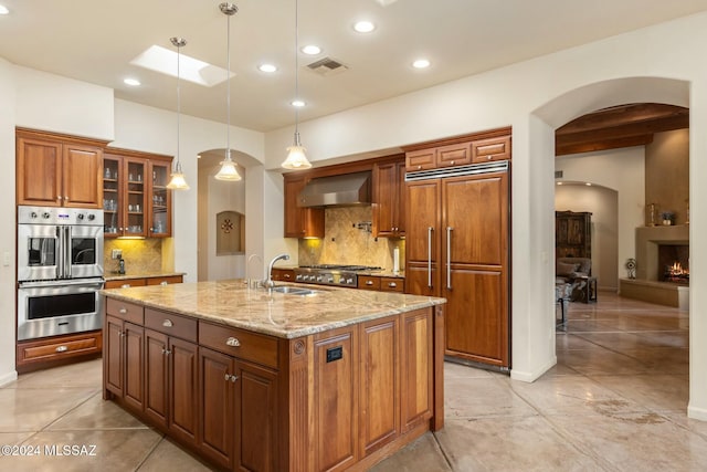 kitchen with pendant lighting, an island with sink, tasteful backsplash, light stone counters, and stainless steel appliances