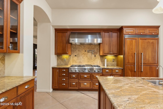 kitchen featuring light stone countertops, stainless steel gas cooktop, wall chimney exhaust hood, and paneled built in fridge