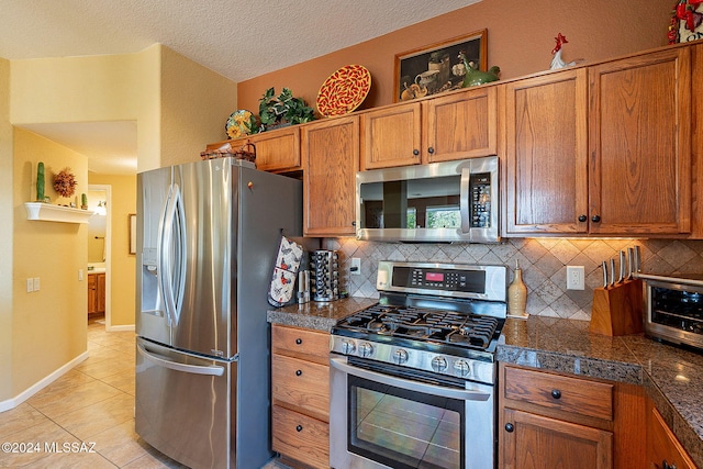 kitchen featuring decorative backsplash, light tile patterned flooring, a textured ceiling, and appliances with stainless steel finishes