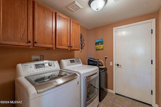 laundry area featuring separate washer and dryer, light tile patterned floors, cabinets, and a textured ceiling