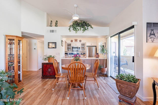 dining room featuring ceiling fan, a towering ceiling, and light hardwood / wood-style floors