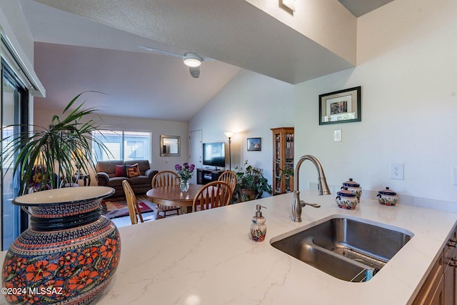 kitchen with a textured ceiling, light stone counters, lofted ceiling, and sink