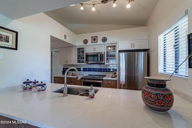 kitchen featuring backsplash, stainless steel appliances, vaulted ceiling, sink, and white cabinets