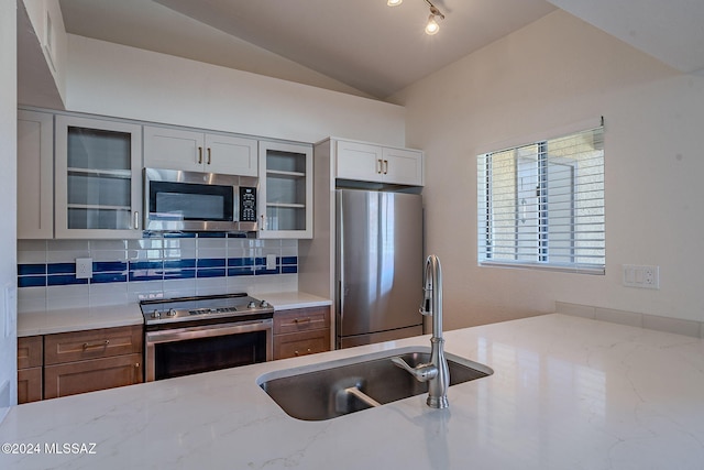 kitchen with light stone countertops, appliances with stainless steel finishes, backsplash, sink, and lofted ceiling