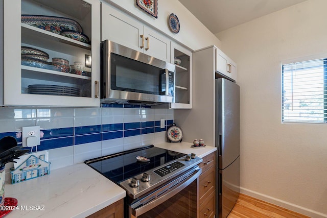 kitchen with white cabinets, decorative backsplash, light stone countertops, light wood-type flooring, and stainless steel appliances