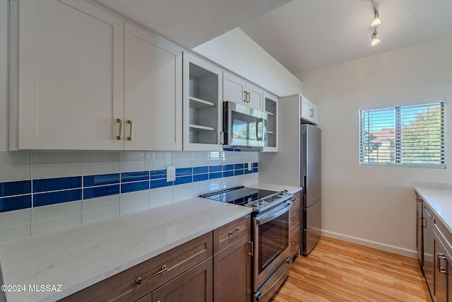 kitchen featuring light stone countertops, tasteful backsplash, light hardwood / wood-style floors, white cabinetry, and stainless steel appliances