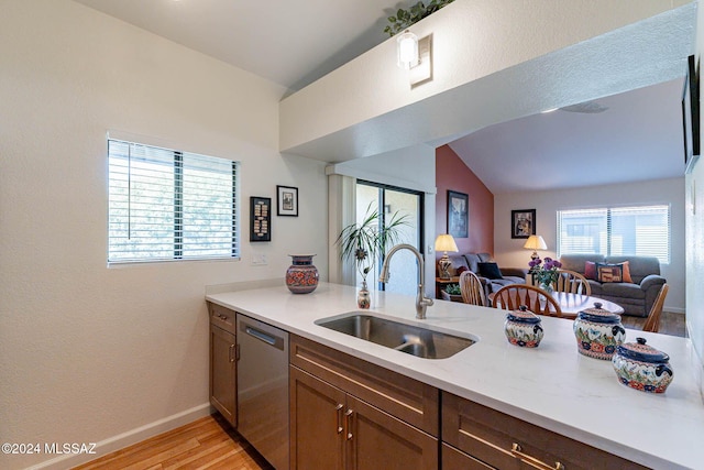 kitchen with sink, light hardwood / wood-style flooring, stainless steel dishwasher, vaulted ceiling, and light stone countertops