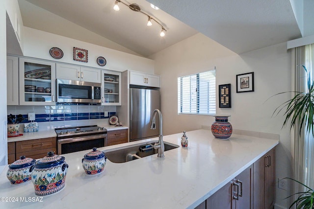 kitchen featuring lofted ceiling, sink, light stone countertops, appliances with stainless steel finishes, and white cabinetry