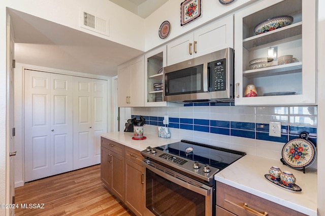 kitchen featuring backsplash, light hardwood / wood-style floors, white cabinetry, and stainless steel appliances