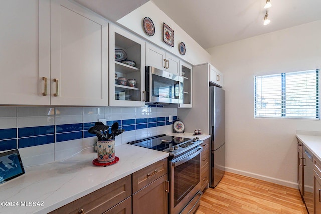 kitchen featuring decorative backsplash, light stone counters, stainless steel appliances, white cabinets, and light hardwood / wood-style floors