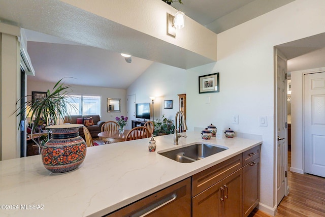 kitchen with kitchen peninsula, light stone counters, vaulted ceiling, sink, and light hardwood / wood-style floors