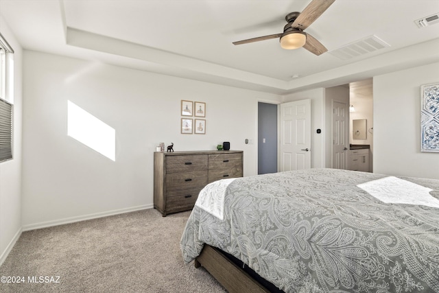 bedroom featuring a raised ceiling, ceiling fan, light colored carpet, and connected bathroom