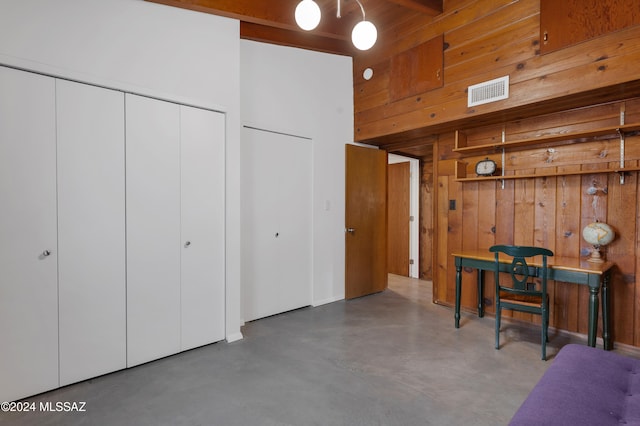 interior space with concrete floors, a high ceiling, wood walls, and beamed ceiling