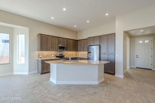 kitchen with backsplash, stainless steel appliances, sink, light tile patterned floors, and an island with sink