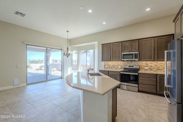 kitchen featuring sink, stainless steel appliances, backsplash, a chandelier, and a center island with sink